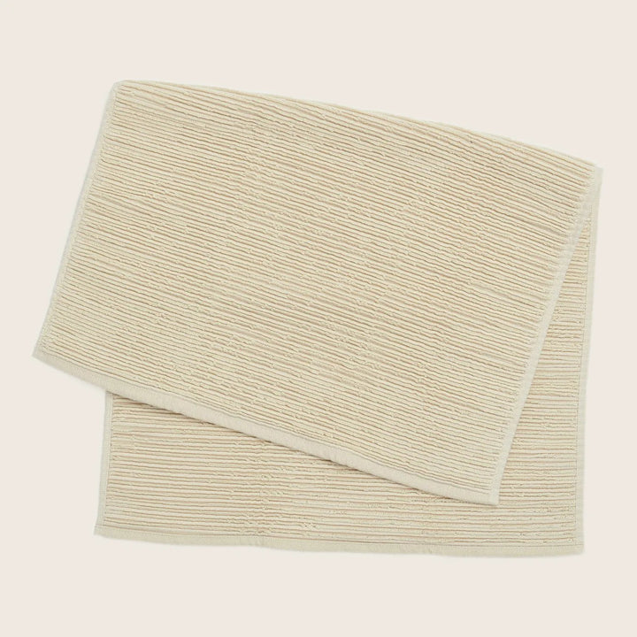 Folded light beige towel with ribbed texture against plain background.