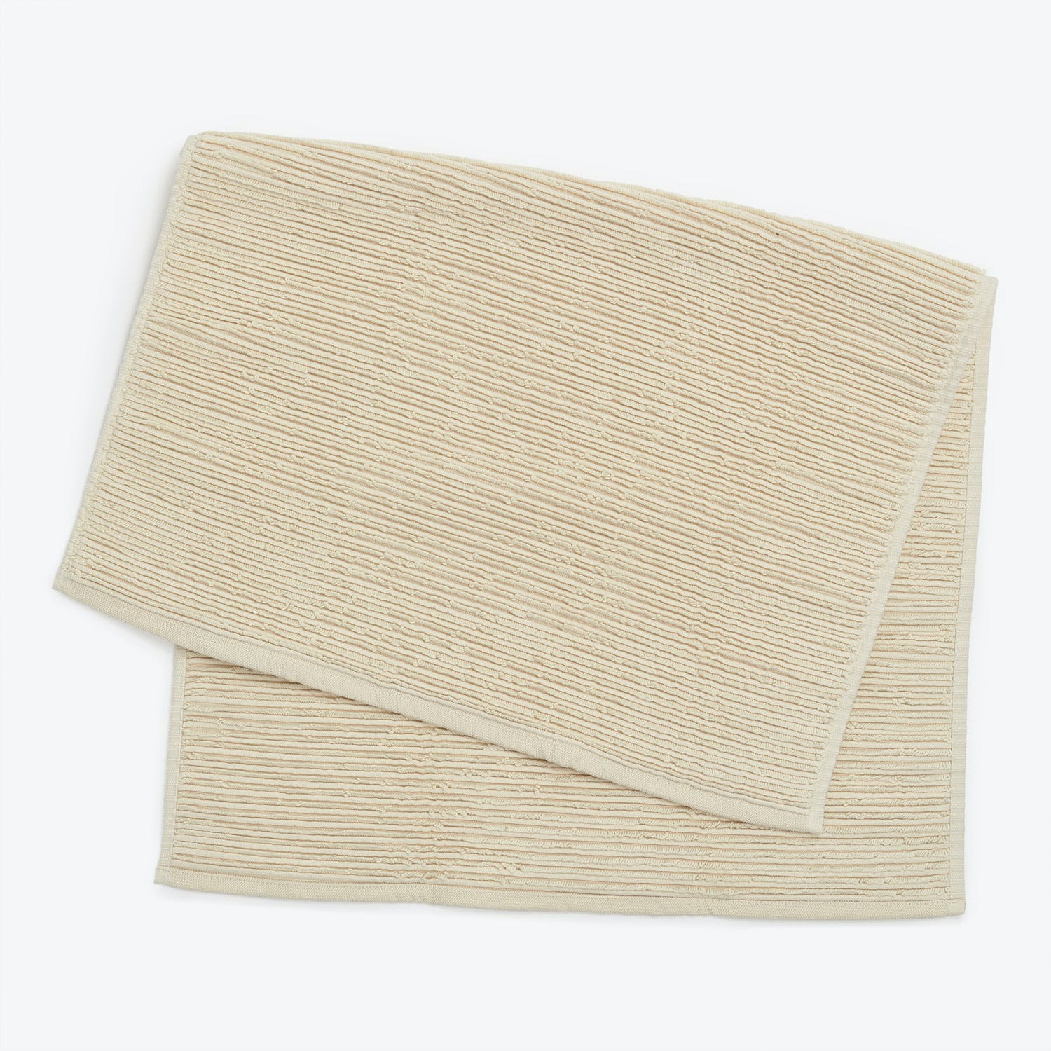 Folded light beige towel with ribbed texture against plain background.