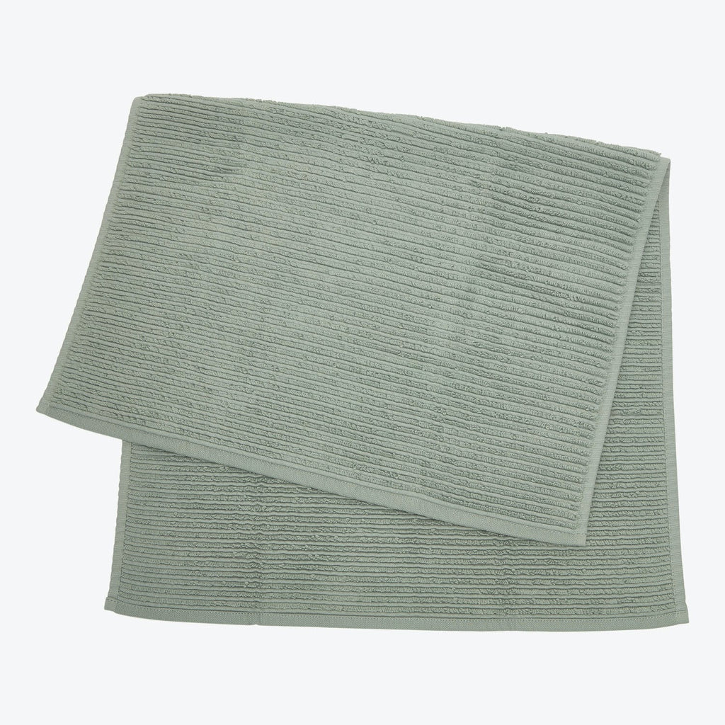 Neatly folded light green bath mat with textured ribbed design.