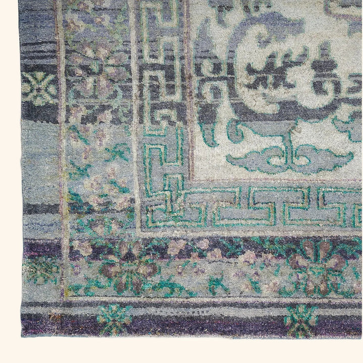 Intricate traditional rug with geometric border and floral motifs, faded colors.