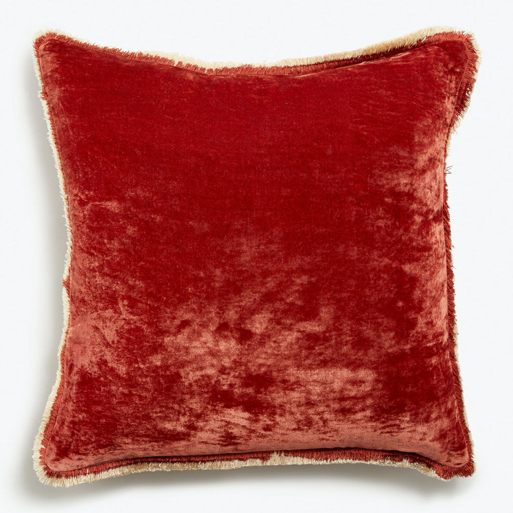 Luxurious crimson velvet pillow with delicate fringe on white background.