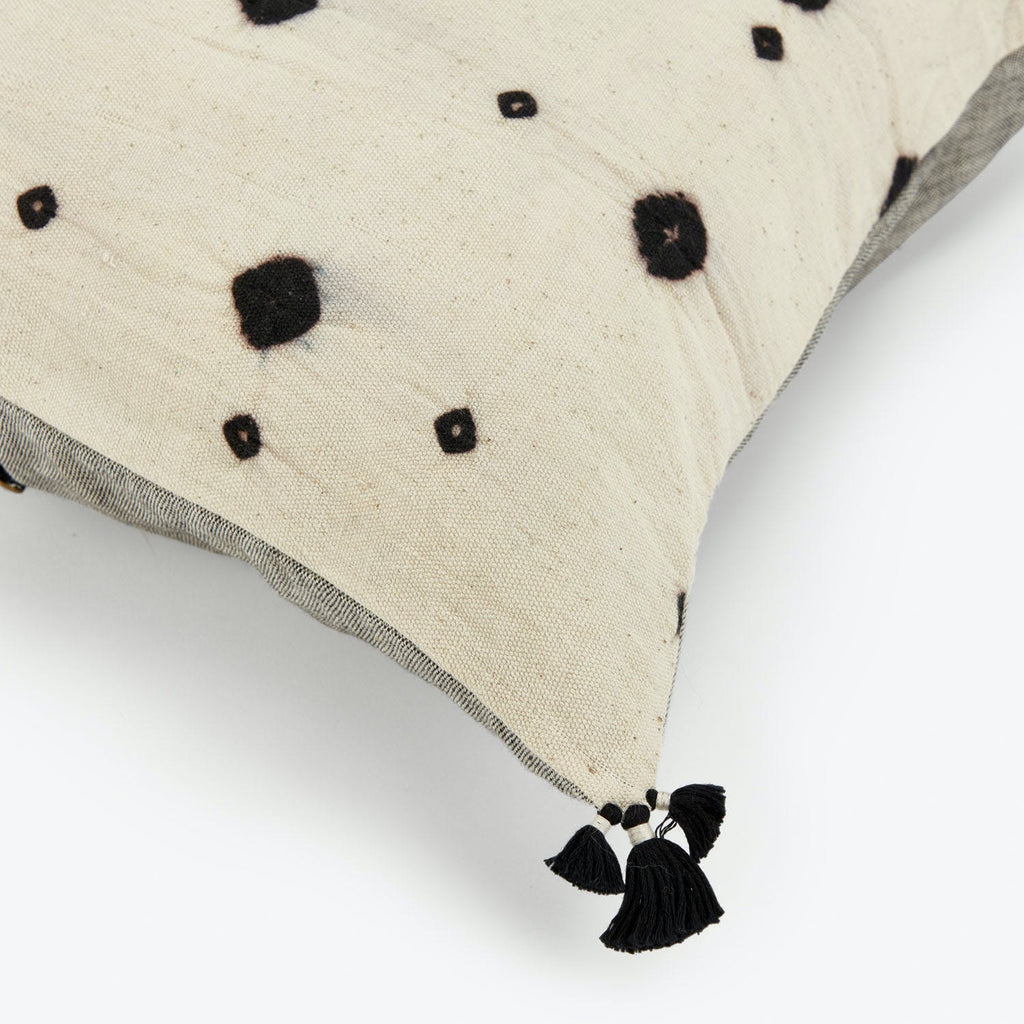 A natural tone decorative pillow with black polka dots and tassels.