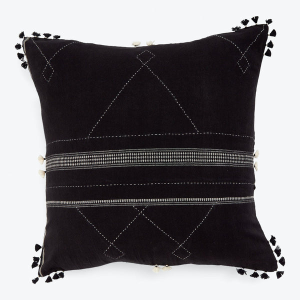 Decorative black pillow with white stitched pattern and playful tassels.