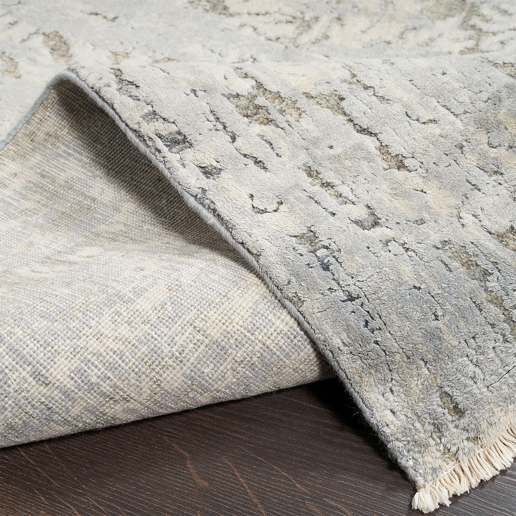 Close-up of a folded rug with intricate grey pattern and fringes on wooden floor