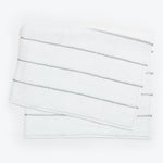 Neatly stacked white towels with embroidered stripes on white background.