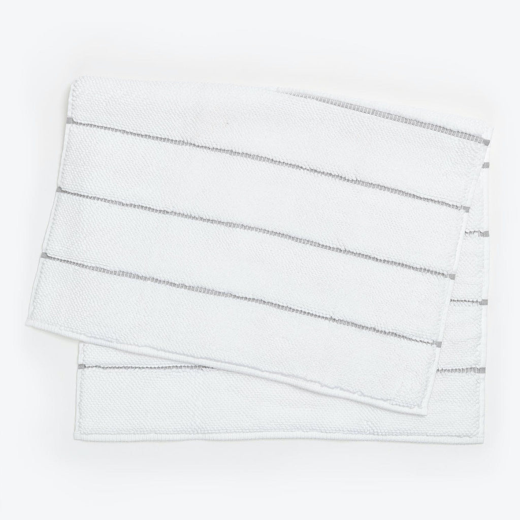 Neatly stacked white towels with embroidered stripes on white background.