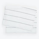 Neatly stacked white towels with embroidered stripes on white background.