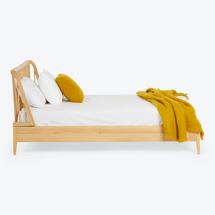 Minimalist and sleek wooden bed with crisp white bedding and pops of mustard-yellow accents.
