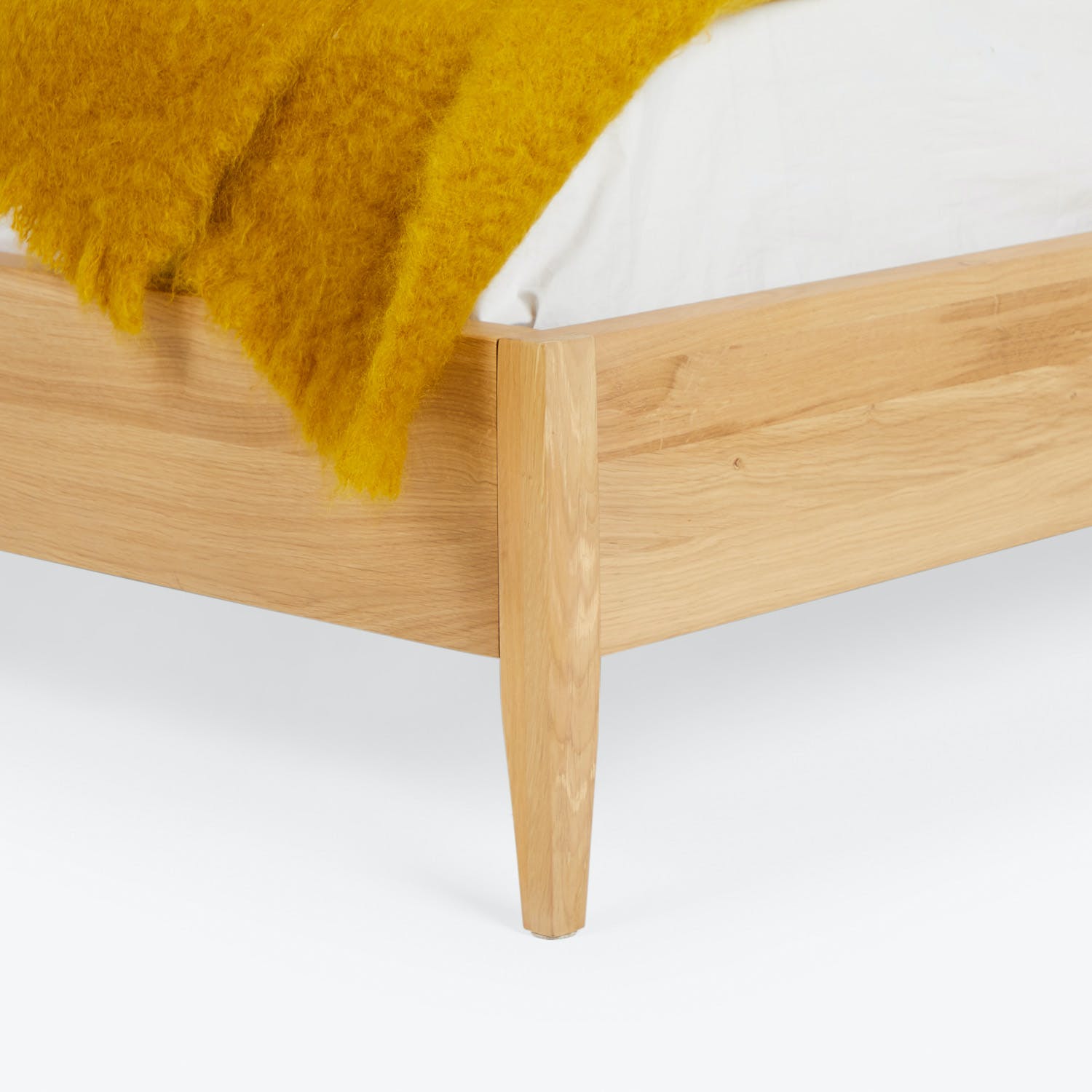 Close-up of modern wooden bed frame with sleek design and yellow blanket.