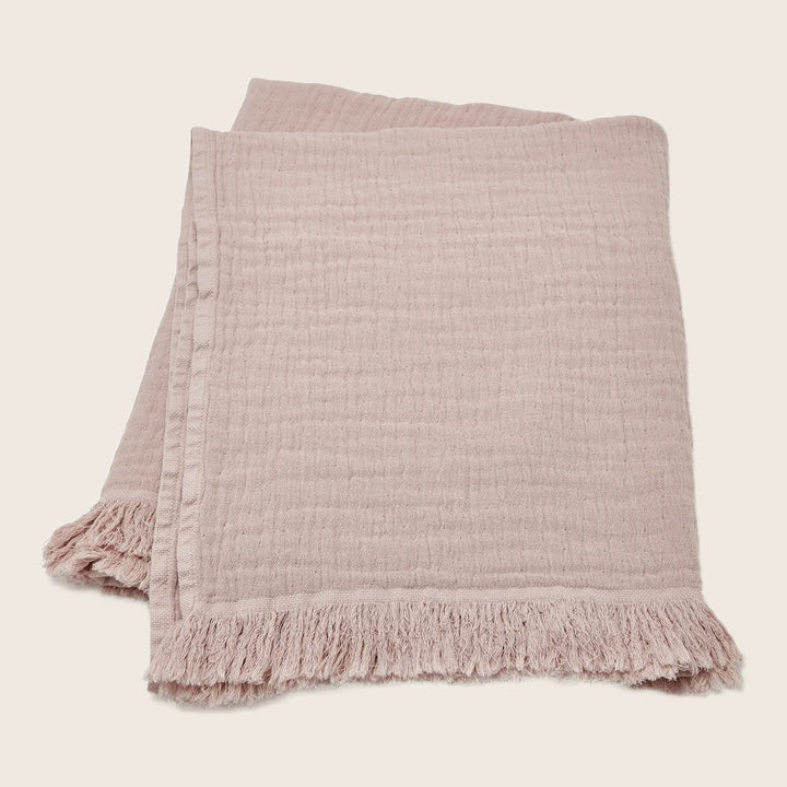 Soft pink throw blanket with delicate texture and fringed edges.