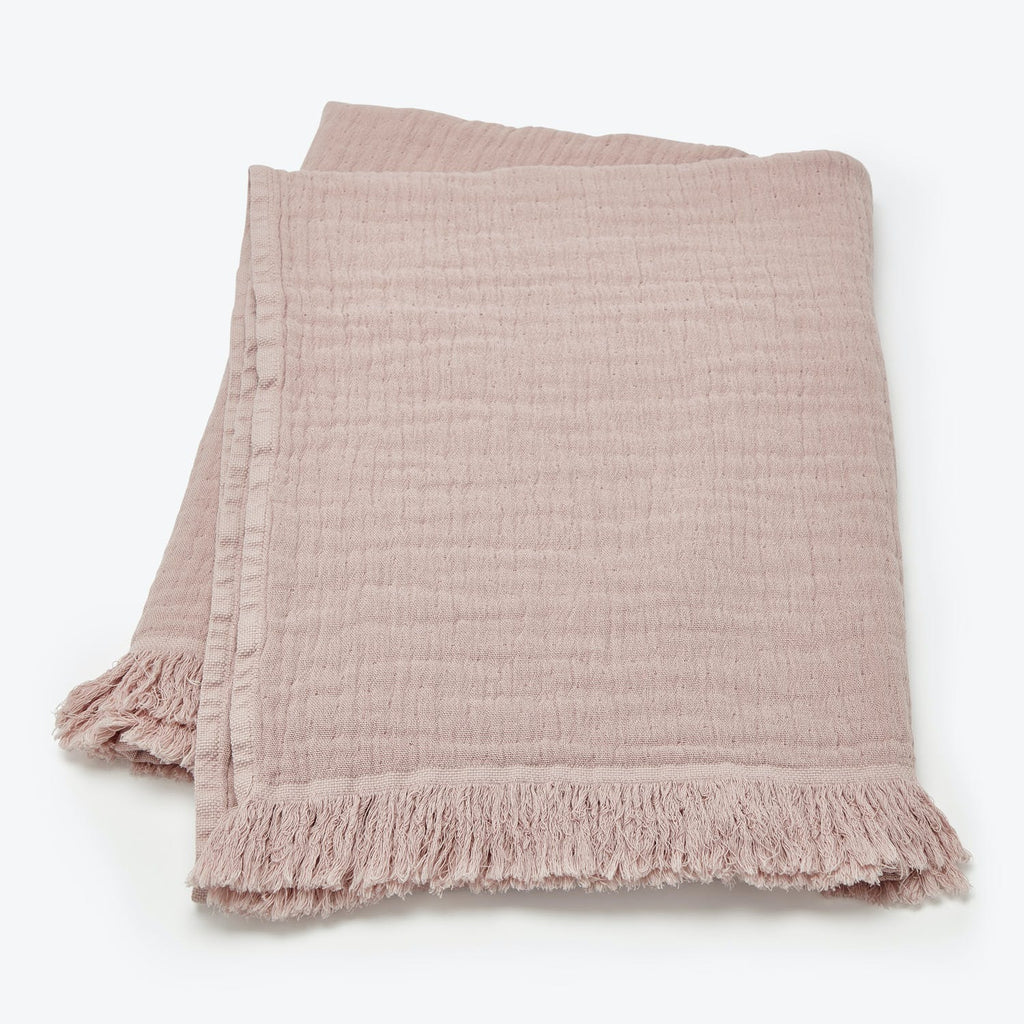 Soft pink throw blanket with delicate texture and fringed edges.
