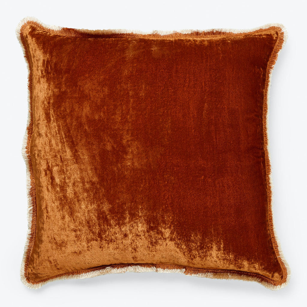 Rust orange velvet square pillow with decorative fringe detail.