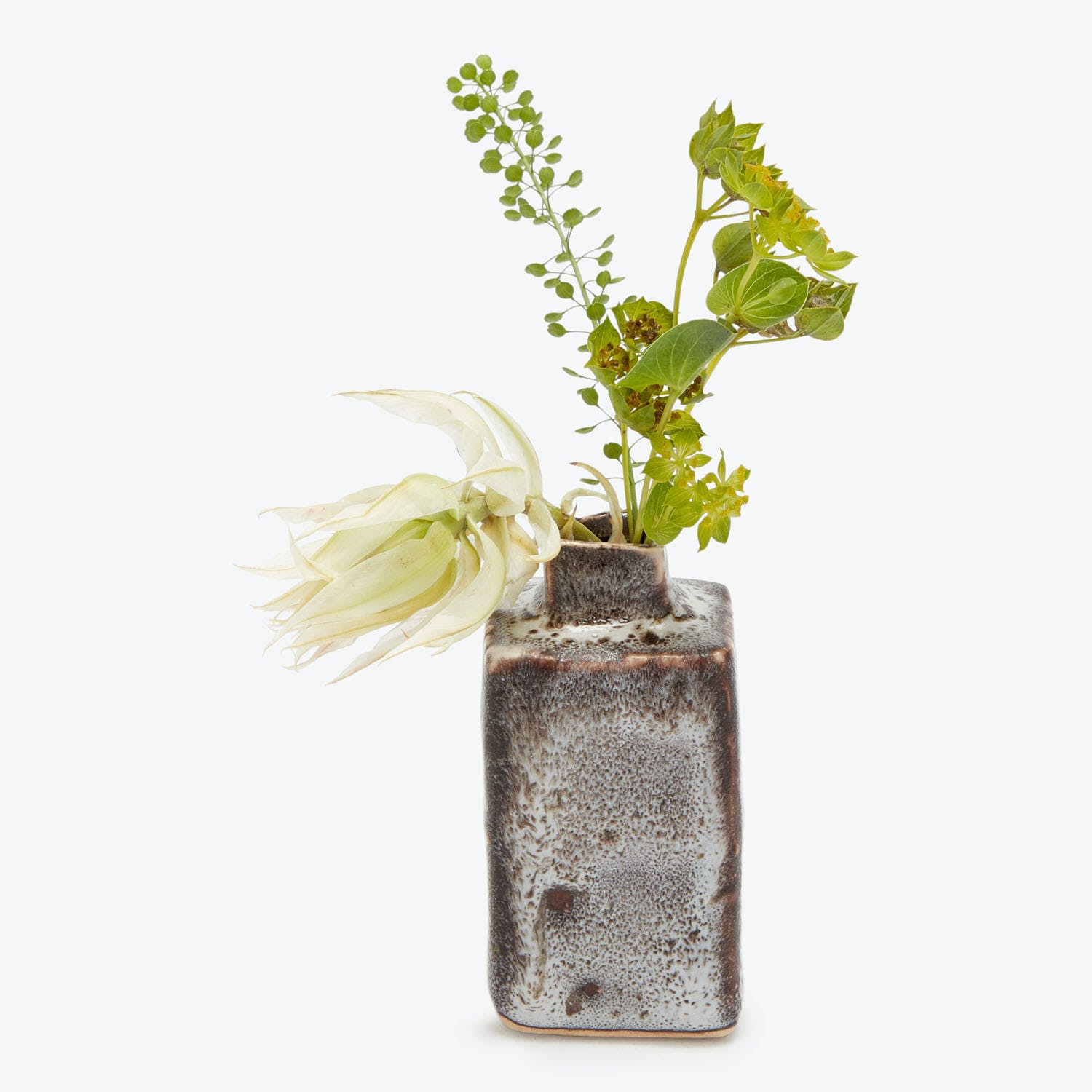 Ceramic vase with distressed glaze holds white flower and greenery.