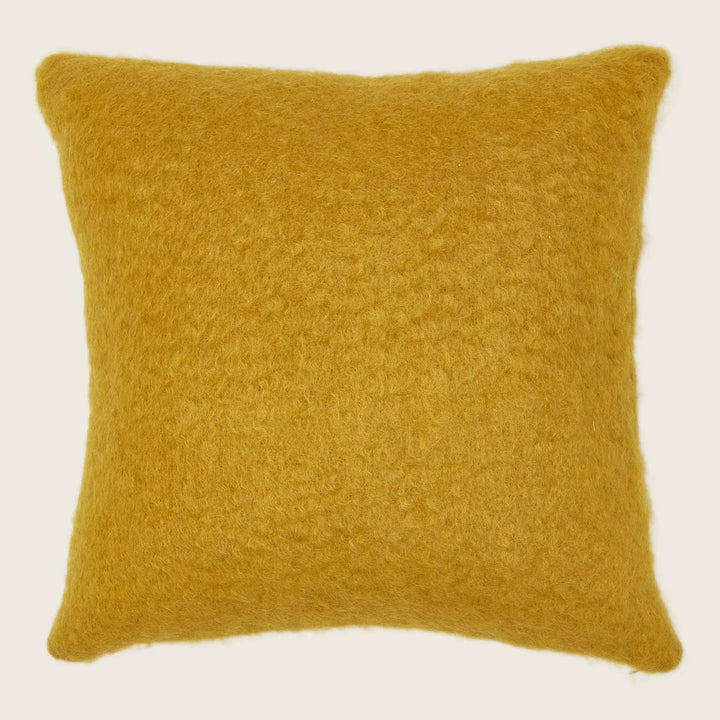 Mustard-colored square pillow with fluffy woolen texture against white background.