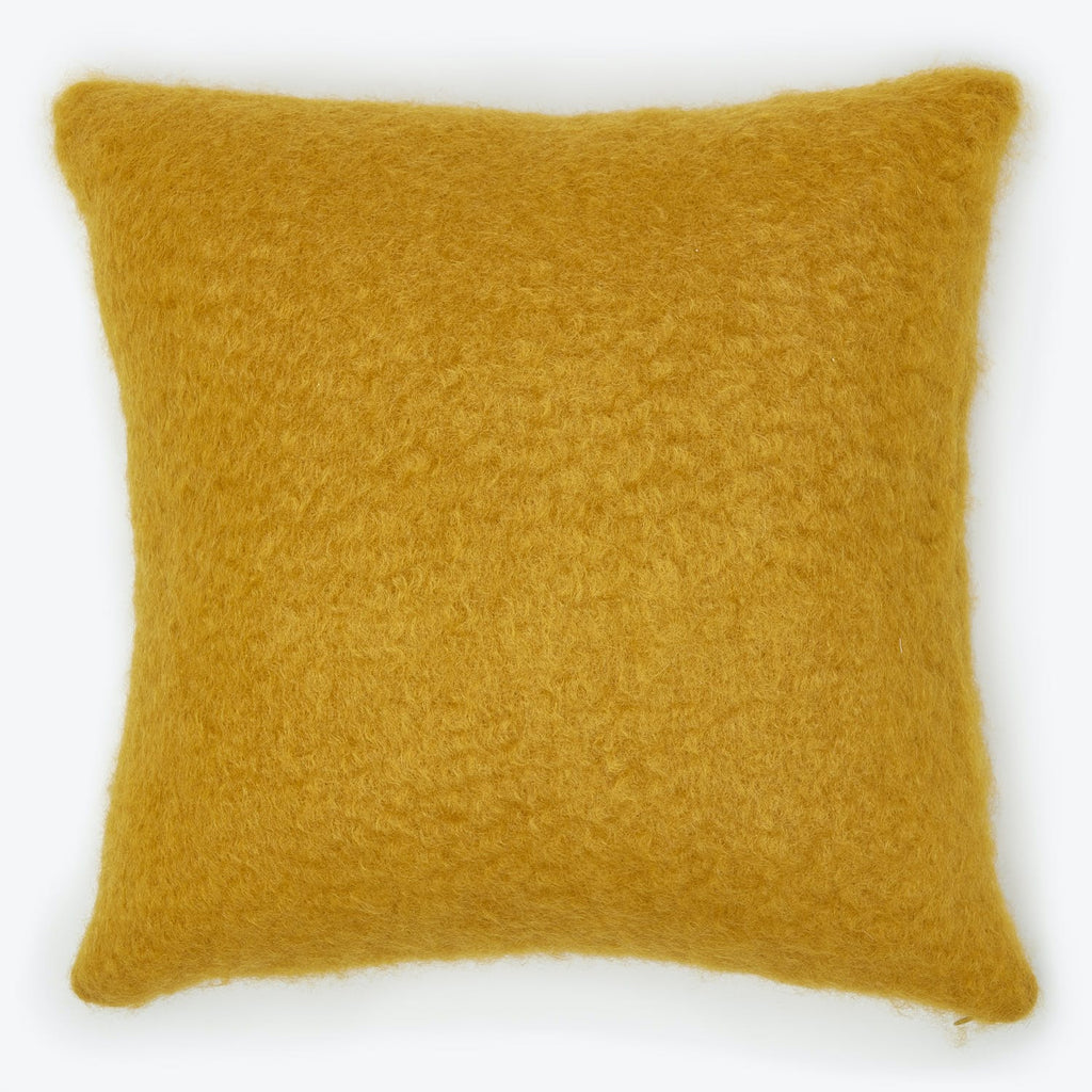 Mustard-colored square pillow with fluffy woolen texture against white background.