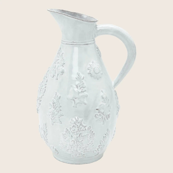 Vintage white ceramic pitcher with intricate floral and leaf patterns.