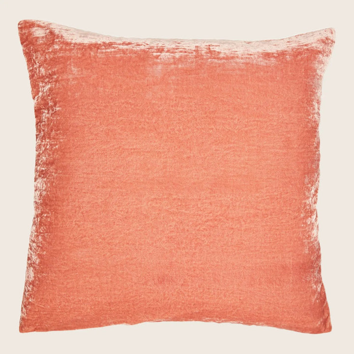 Square coral pillow with textured velvet-like surface on white background.