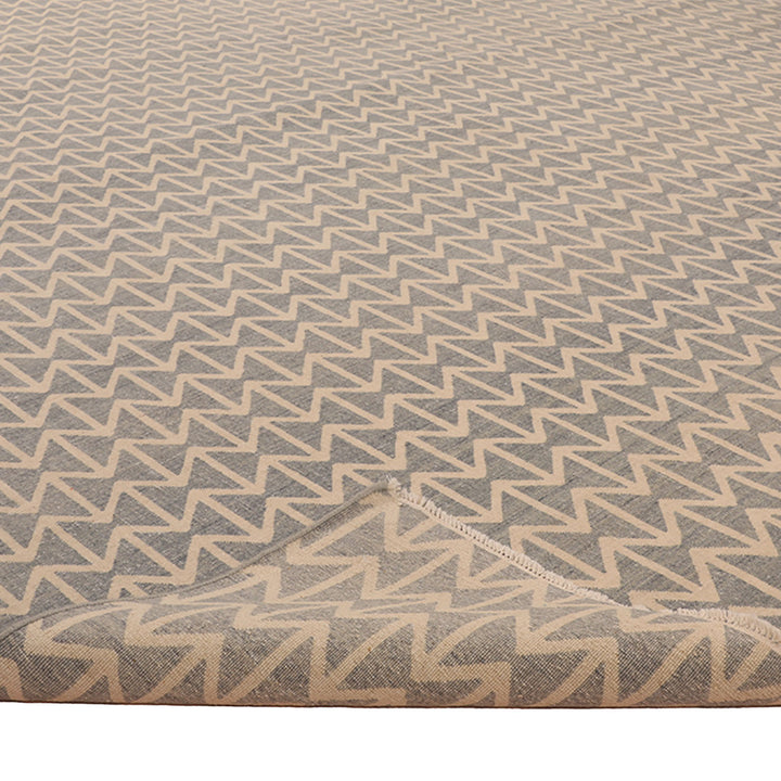 Flat textile rug with geometric pattern in beige and gray.