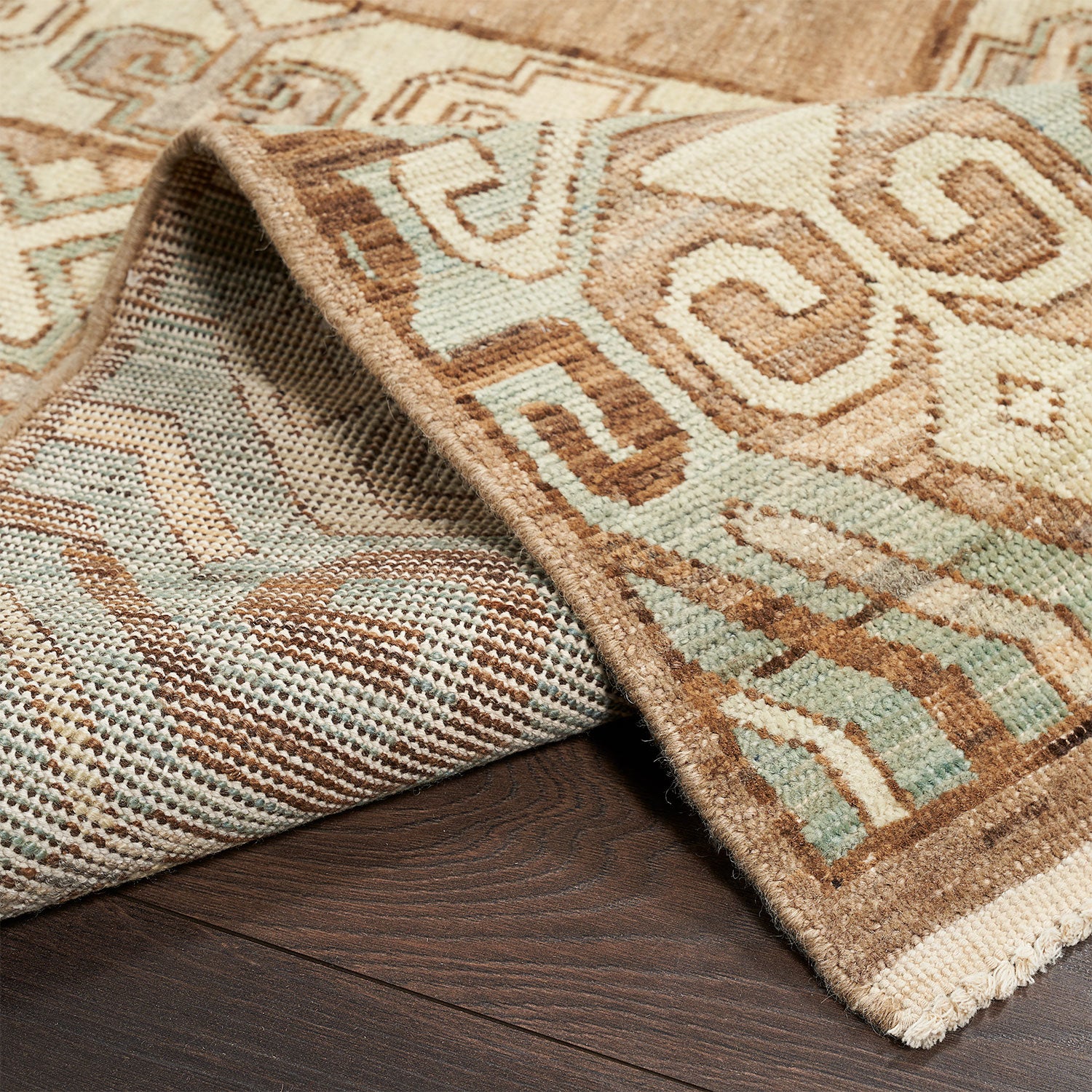 Intricate patterned rug with folded corner showcases traditional ethnic motif.