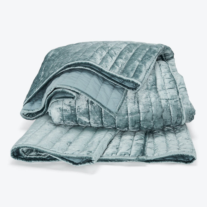 Folded plush teal blanket with quilted details and velvety texture.