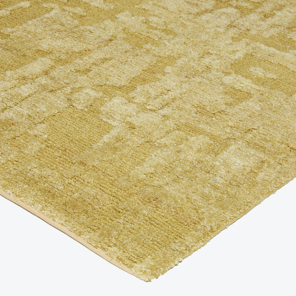 Close-up of a golden carpet with regular geometric textured pattern.
