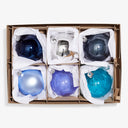 Set of six colorful Christmas baubles individually wrapped in white paper.