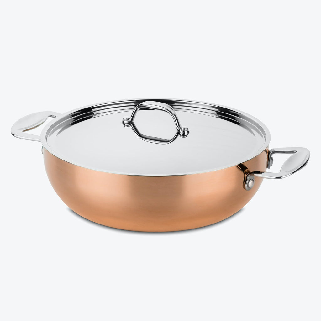 A shiny copper sauté pan with a silver lid and handles.