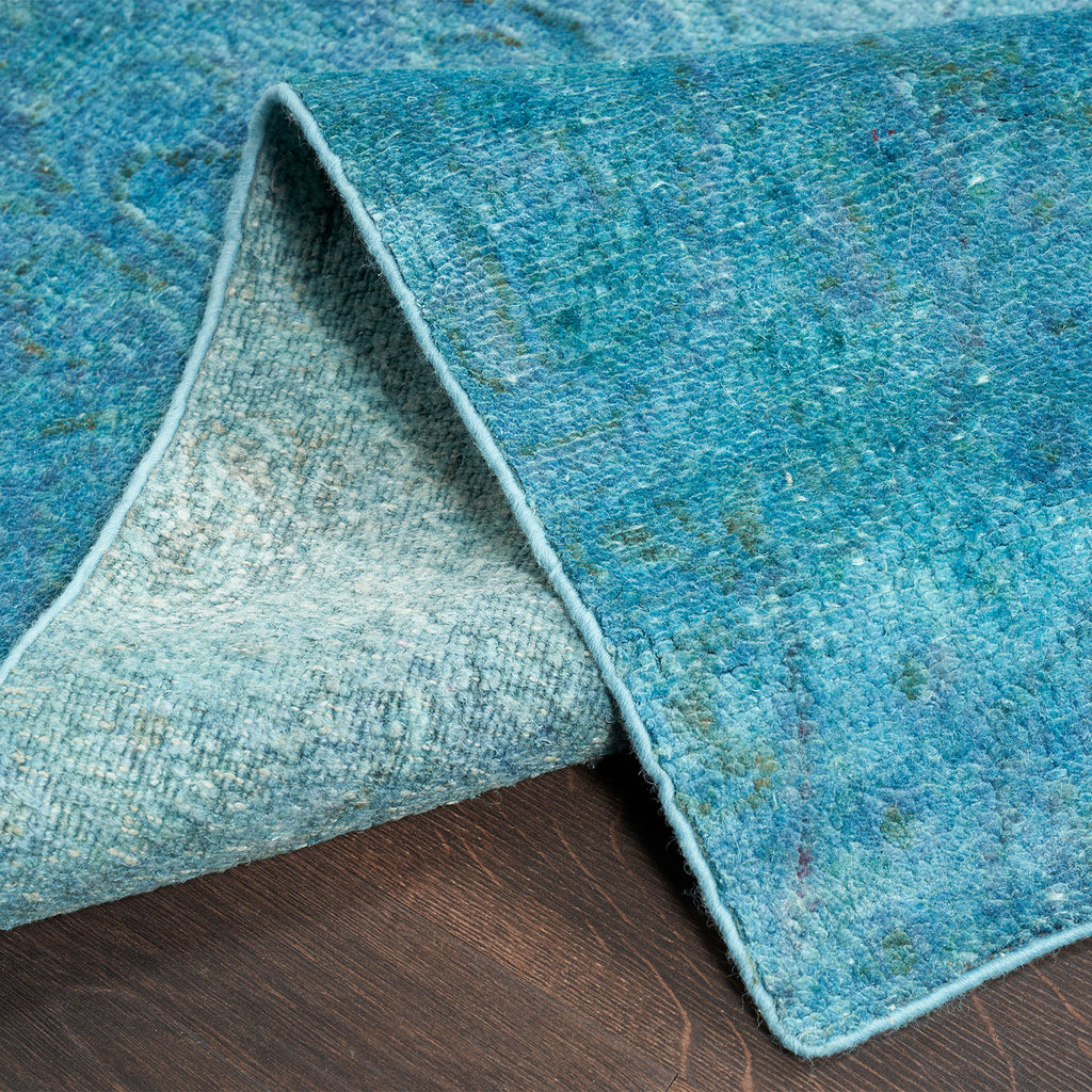 Folded corner of textured blue rug resting on wooden floor