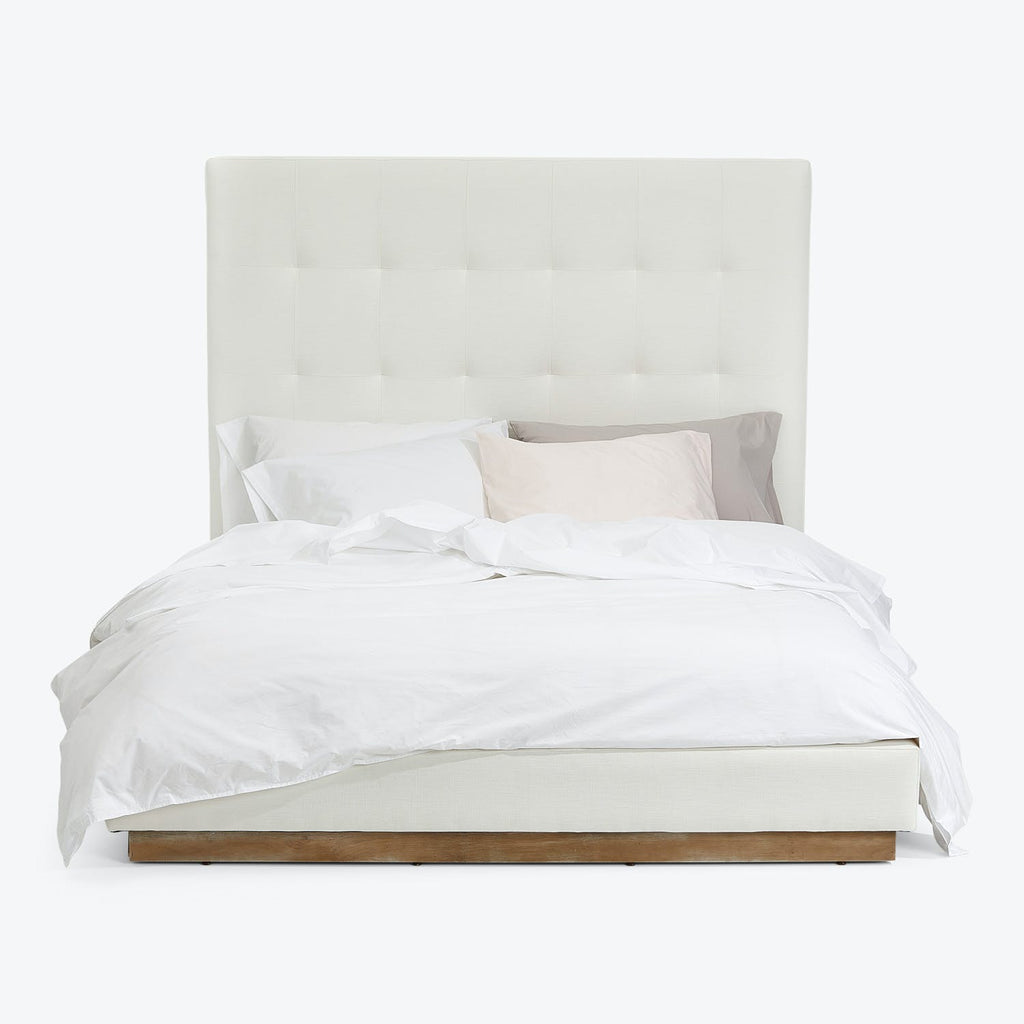 Neatly made bed with white upholstered headboard and tufted design.