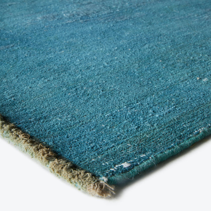 Blue carpet with dense pile, bound edges, showing minor wear.