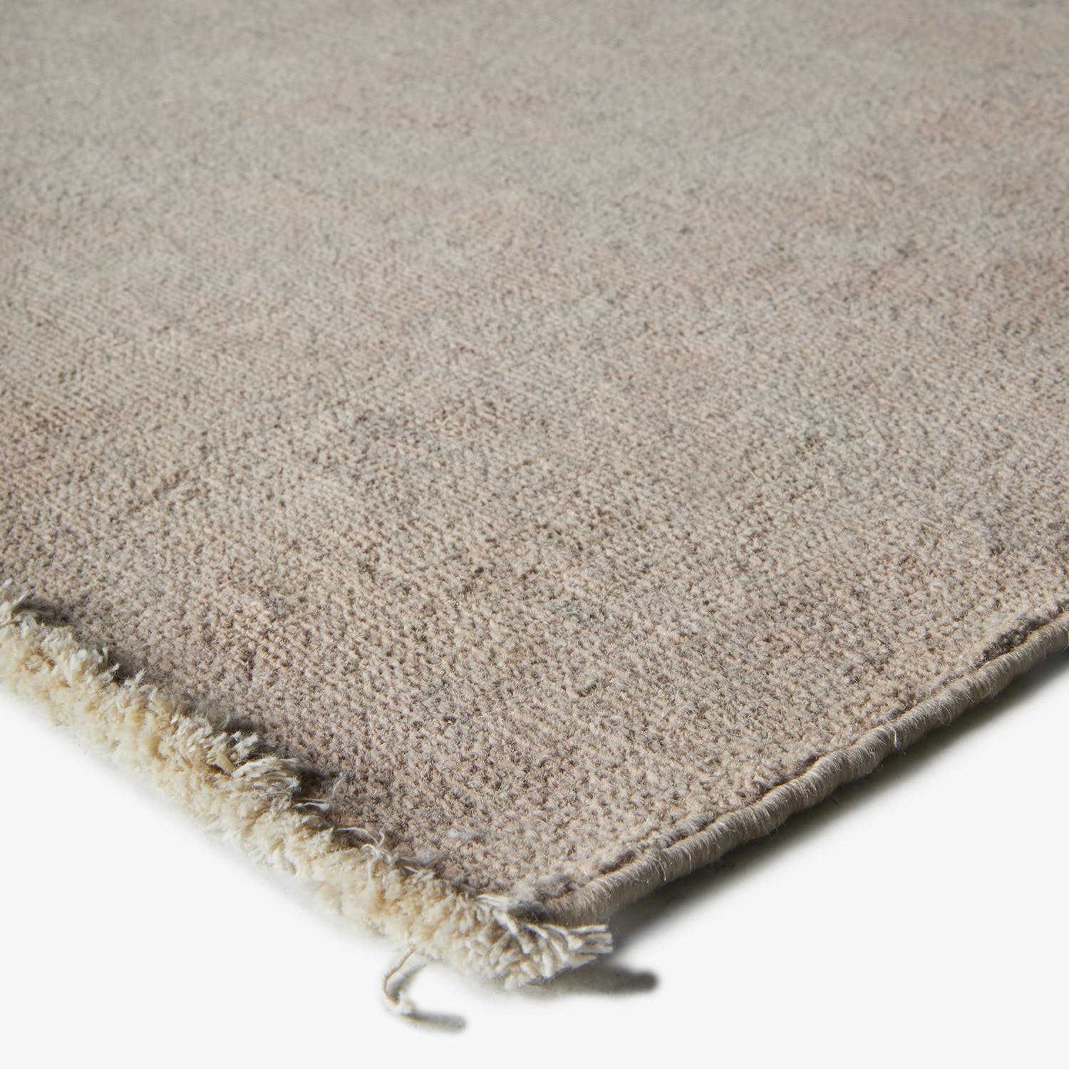 Close-up of a neutral-colored rug with a worn fringed border.