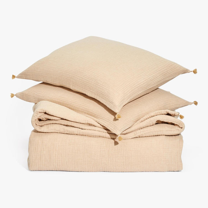 Neutral sandy-beige bed linens with tassel pillows on canvas-like texture.