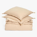 Neutral sandy-beige bed linens with tassel pillows on canvas-like texture.