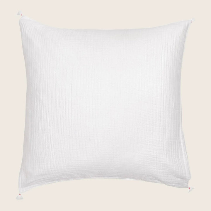 White square pillow with waffle-like weave and pink pom-pom corners.