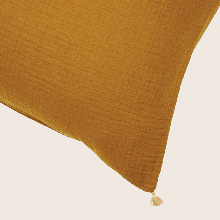 Close-up of a mustard yellow textured pillow with tassel detail.