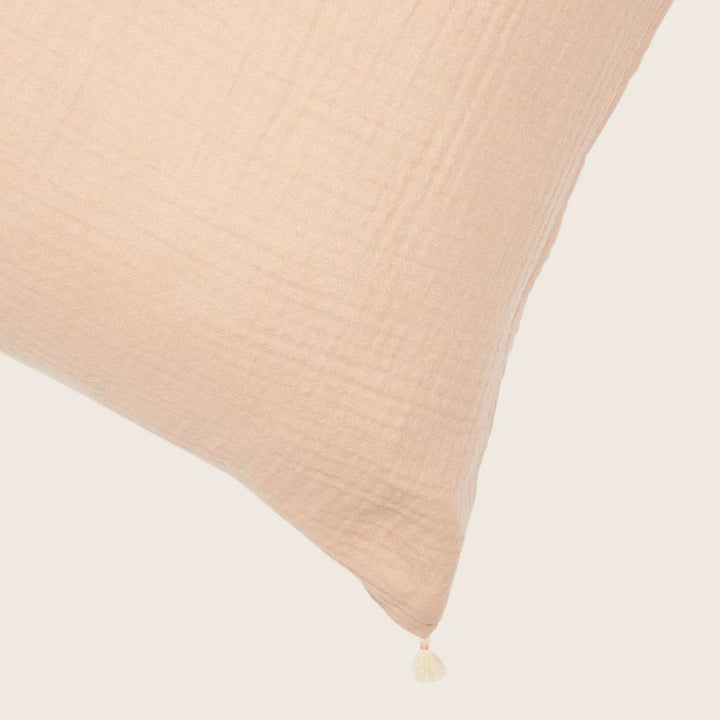 Blush pink linen cushion with crinkled texture and decorative tassel.