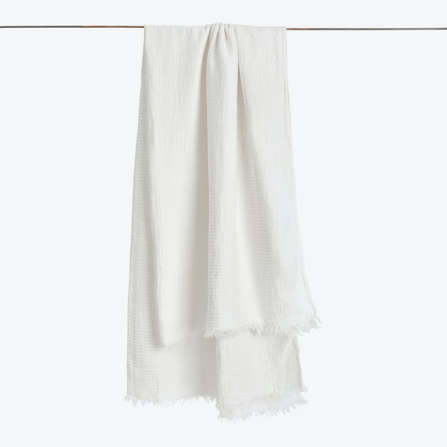 White textured towel with fringe hanging on straight horizontal rod.