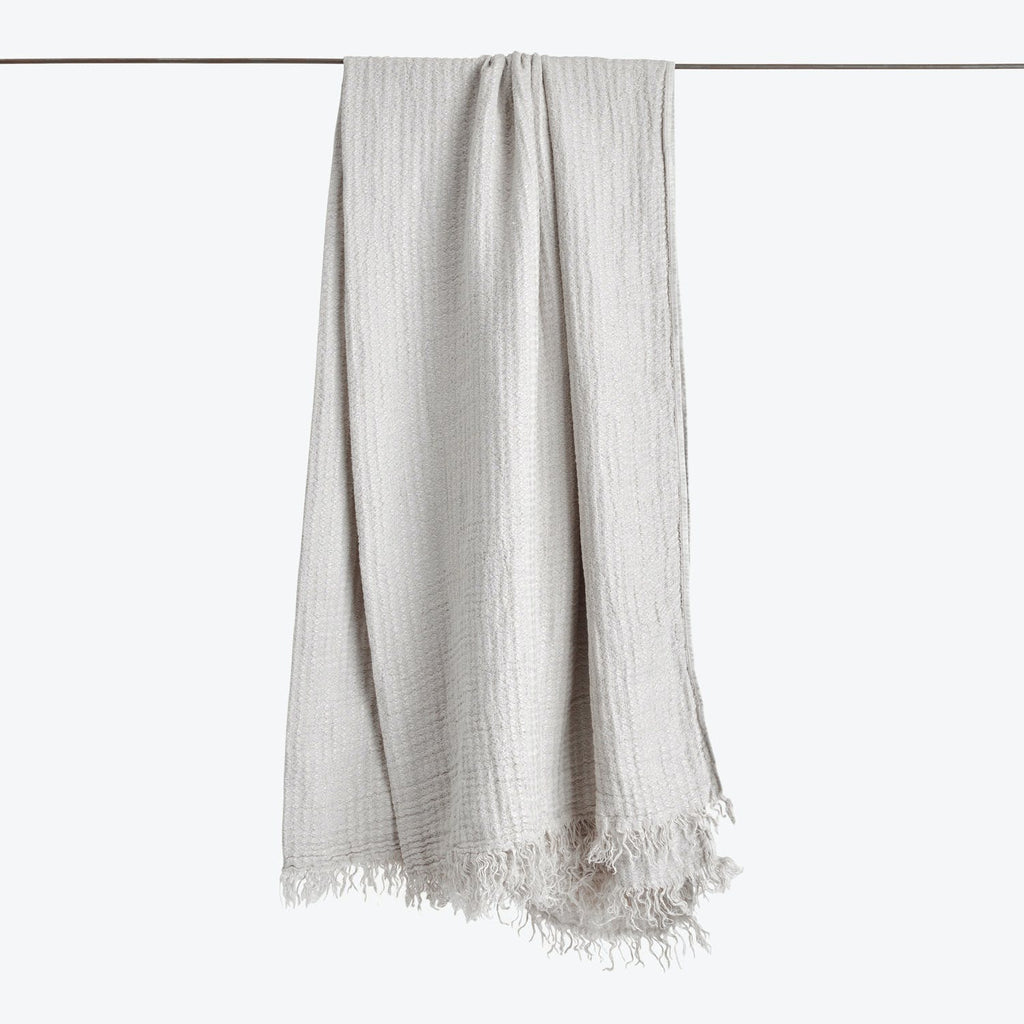 Light-colored fabric with subtle pattern and fringe detailing, hanging vertically.