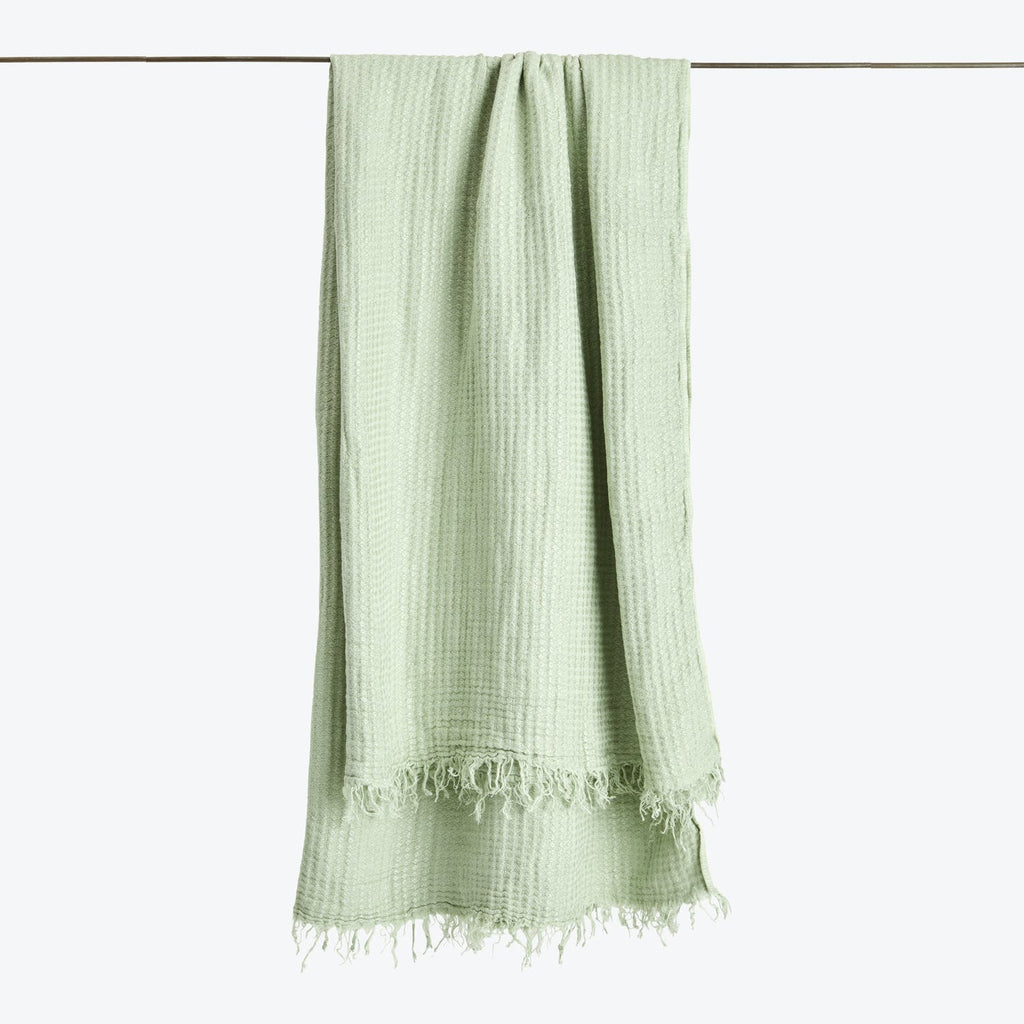 A light green textile with a textured weave and fringed edge.