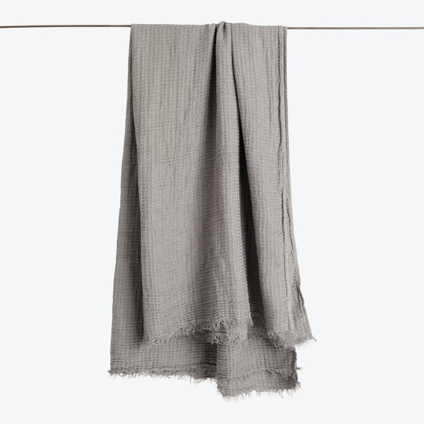 Gray woven fabric with textured weave and fringed edges displayed