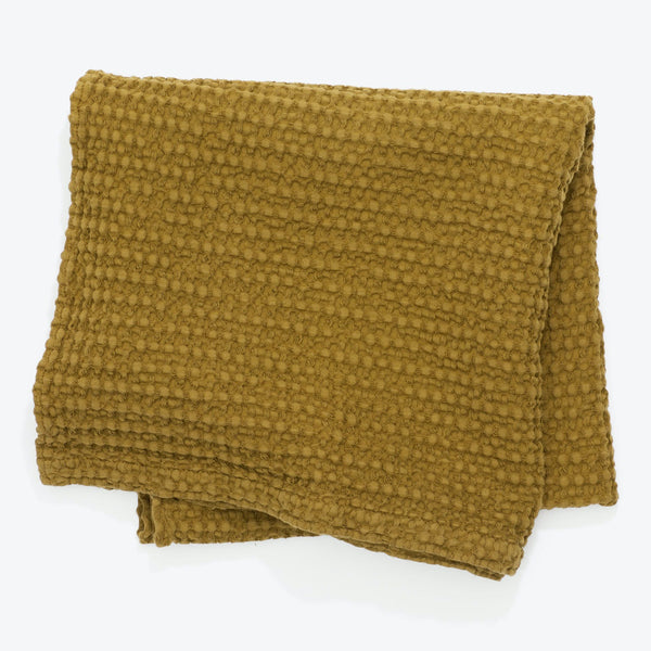 Folded olive green or mustard textile with plush bobbled texture.
