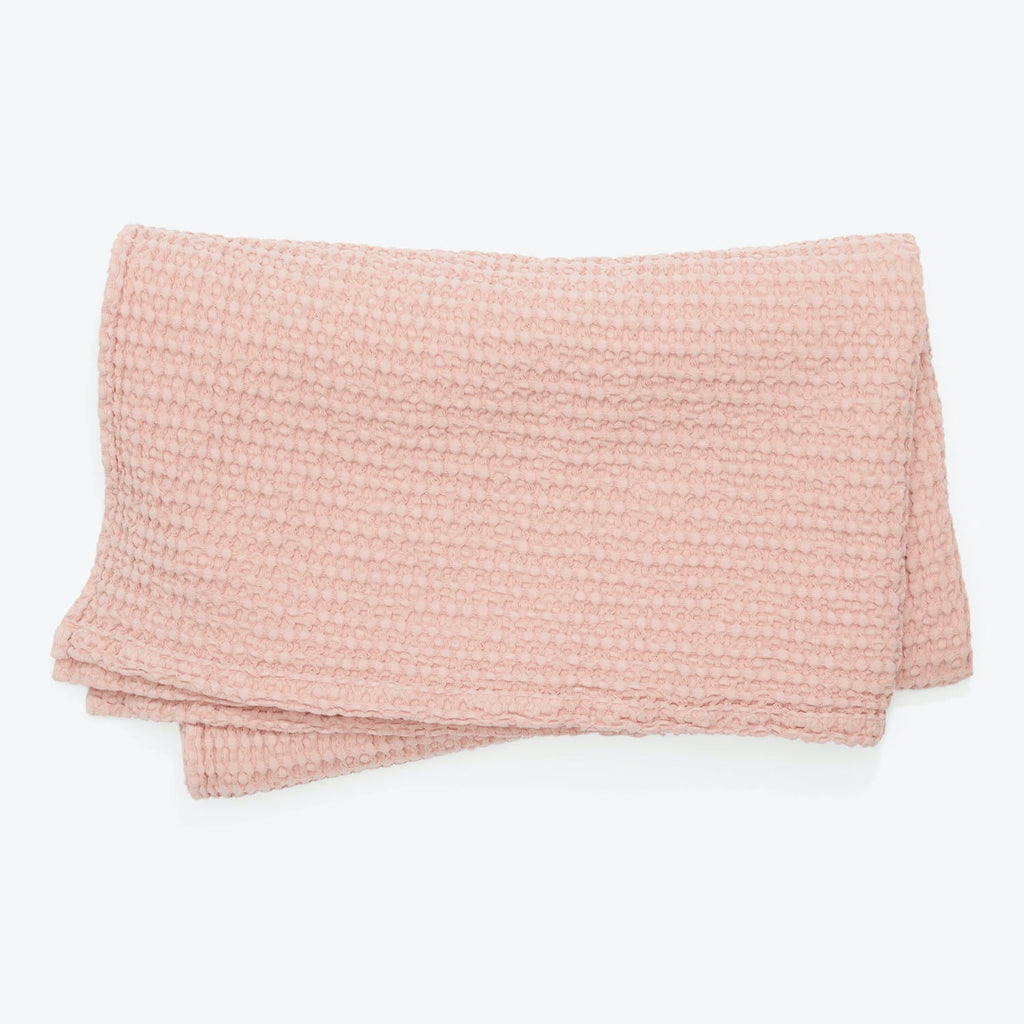 Pale pink knit blanket with soft textured loops neatly folded.