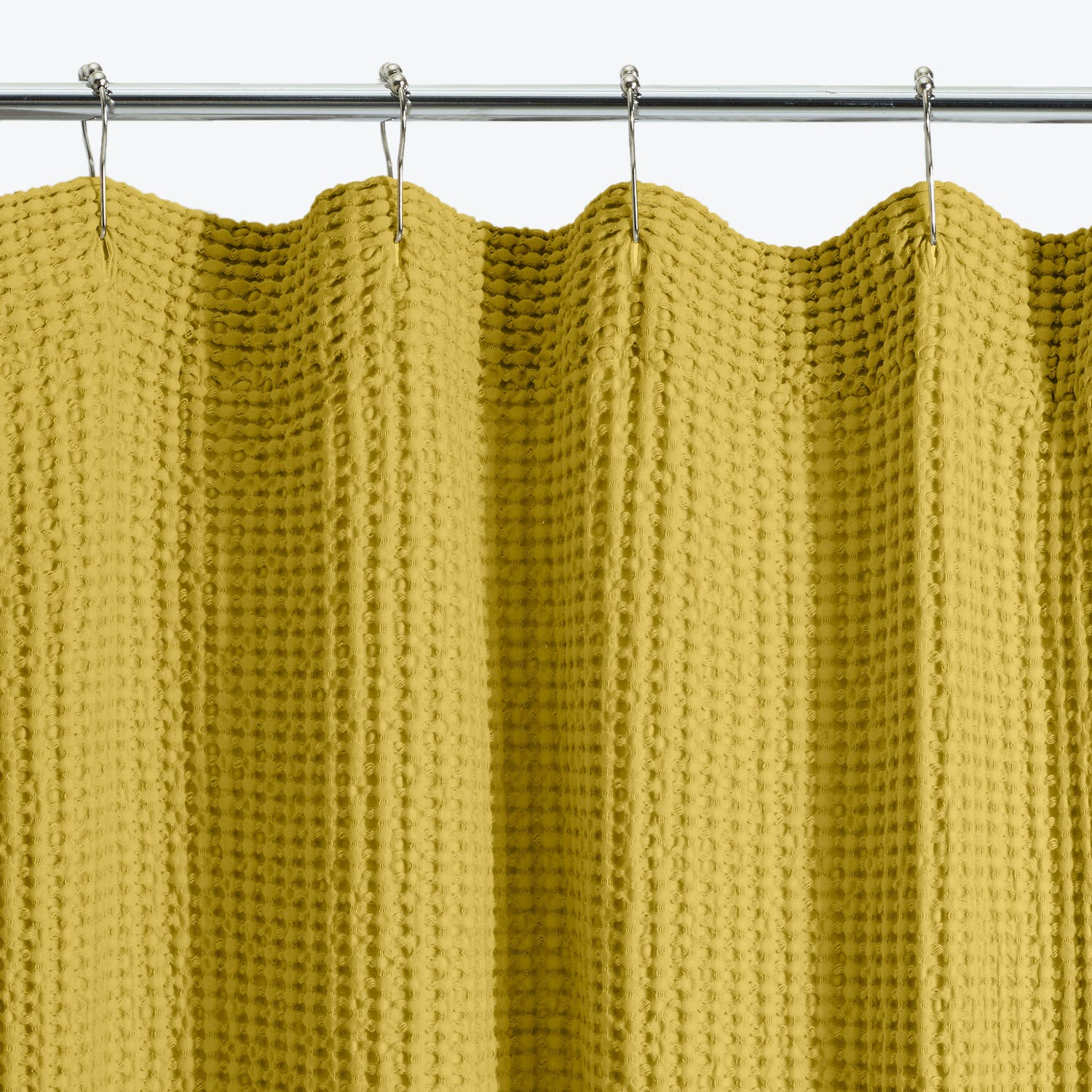 Yellow textured curtain with knitted-like pattern hangs on metal rod.