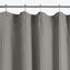 Gray knitted curtain with textured pattern hangs on curtain rod.