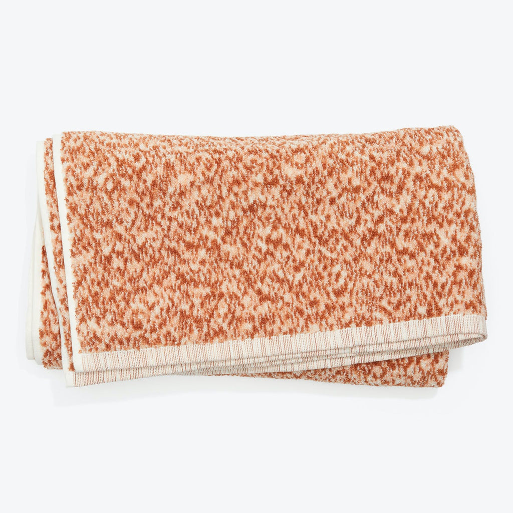 Folded terrycloth towel with orange speckles and striped binding.