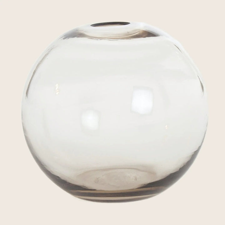 Round, transparent glass vase with smoky tint and reflective surface.