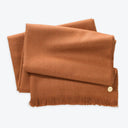 Rusty brown woolen scarf with fringe and decorative button detail.