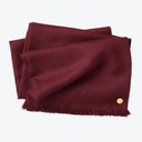 Burgundy fabric with fringes and button for scale on white background.