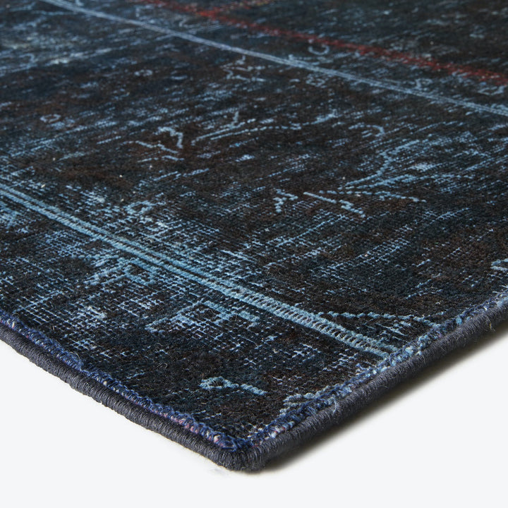 Close-up of a distressed, abstract rug with dark hues and intricate pattern.
