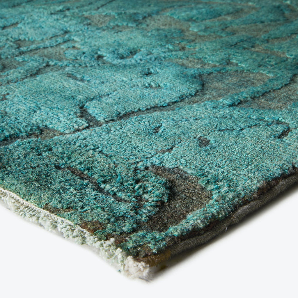 Close-up of a textured rug corner with intricate turquoise pattern.